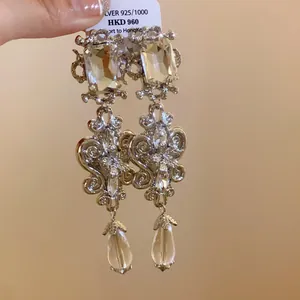 Detail of ornate silver dangle earrings with square crystals and teardrop pendants.