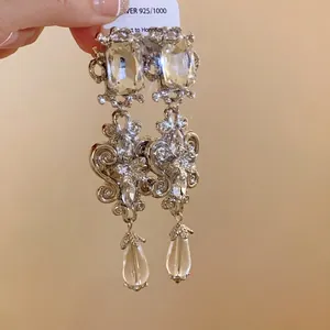 Close-up of ornate silver dangle earrings with crystals and clear teardrop pendants