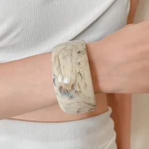 Detailed close-up view of a wide marbled acetate bangle bracelet worn on a woman's wrist