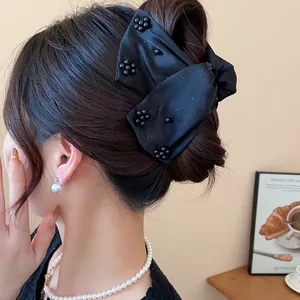 Detail view of a large black fabric bow hair claw clip worn on a woman's bun hair style.