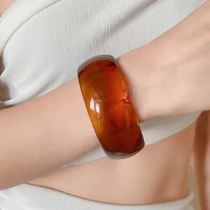 Close-up view of a minimalist amber marbled resin bangle worn on a woman's slender wrist