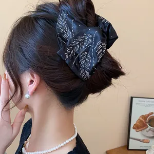 Detail view of a large black fabric hair claw clip decorated with silver rhinestones
