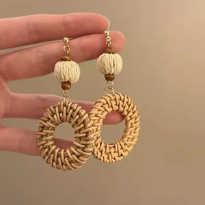 Détail de boucles d'oreilles en raphia avec perles en bois et clous dorés