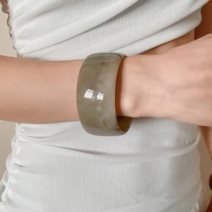 Detailed view of a wide marbled resin bangle with amber swirls on a woman's wrist.