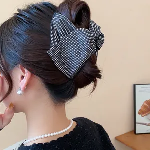 Close-up detail of a large black rhinestone bow hair claw clip worn by a model for a bun style