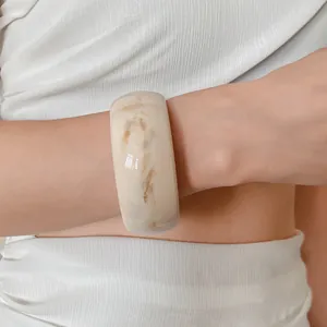 Close-up view of a marbled cream and brown wide resin bangle worn on a model's wrist
