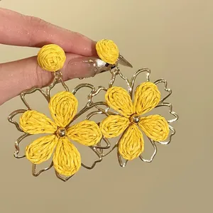 Gros plan détaillé de boucles d'oreilles fleur en raphia jaune avec cadre doré