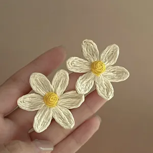 Vue rapprochée de boucles d'oreilles marguerites en raphia faites à la main avec pétales blancs