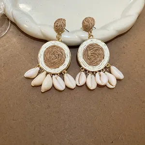 Détail des boucles d'oreilles pendantes en raphia tissé avec coquillages blancs cowrie