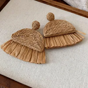 Gros plan détaillé de la texture tissée main de ces boucles d'oreilles en raphia naturel.