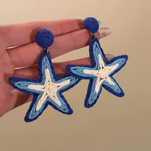 Gros plan de boucles d'oreilles étoile de mer en raphia bleu et blanc