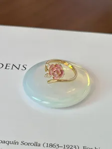 Dettaglio di un anello rosa in smalto con pietre luccicanti su sfondo di un libro d'arte.