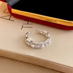 Elegante anillo abierto en forma de onda con circonitas y perlas en una caja de lujo