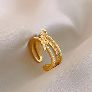 Dettaglio di un anello regolabile in oro con un fiocco di perle e fasce incastonate di zirconi.