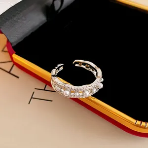 Detalle de cerca de anillo abierto con diseño de onda, circonitas y perlas finas