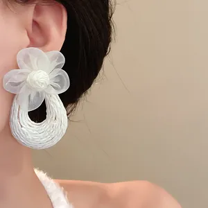 Close-up detail of white mesh flower earrings with woven drop on an Asian model.