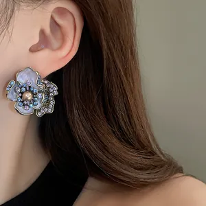 Close-up of retro floral stud earring with blue rhinestones and pearl on model