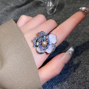 Macro view of vintage flower ring featuring blue rhinestones and a central pearl on a finger