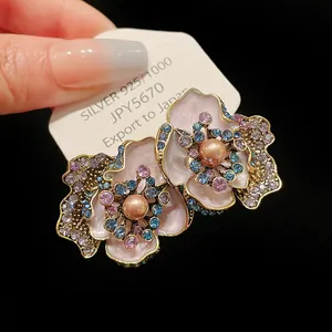 Close-up of vintage flower earrings with pink enamel, pearls, and colorful rhinestones.