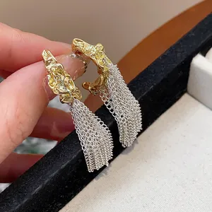 Close-up of silver needle tassel earrings with gold lava texture and silver chains.