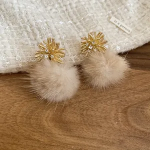 Macro detail of elegant golden flower stud earrings featuring soft beige faux fur pom-poms