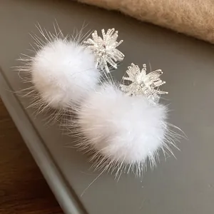 Detailed close-up of white fluffy pompom earrings with elegant silver starburst design