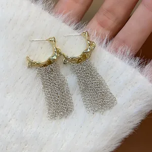 Close-up detail of silver needle tassel earrings with gold-toned hoop and fringe chain