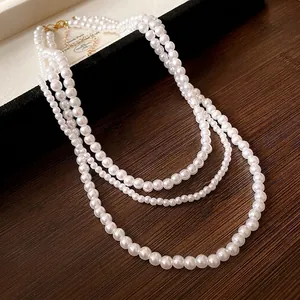 Elegante collana di perle finte a più strati con chiusura a moschettone dorata.