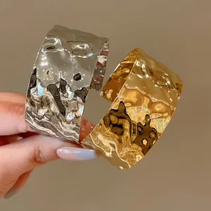 Dettaglio di due bracciali rigidi aperti in metallo con finitura stropicciata irregolare