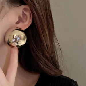 Detail view of a large polished gold metallic hemispherical stud earring worn on the ear
