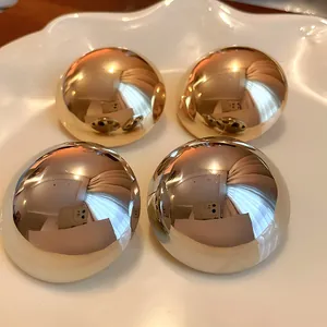 Close-up detail of polished gold and silver metallic dome stud earrings on a plate