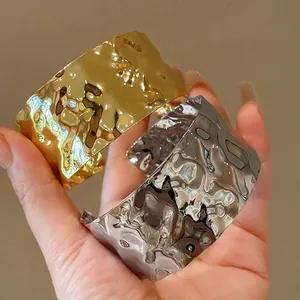 Dettaglio di bracciali rigidi aperti irregolari in metallo martellato oro e argento