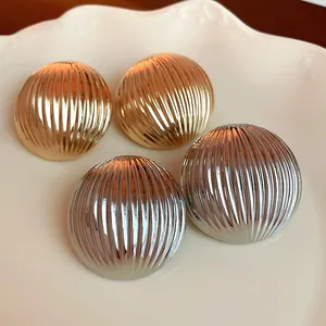 Macro detail of metallic ribbed dome earrings in gold and silver finish on white plate
