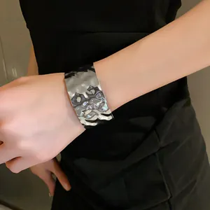 Primo piano di un bracciale a fascia larga argentato con trama plissettata irregolare