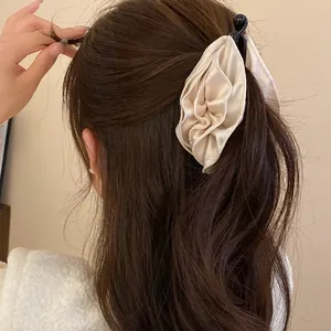 Dettaglio di un'elegante molletta per capelli con fiore in tessuto plissettato crema