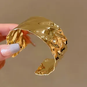Primo piano di un bracciale a polsino dorato con trama a pieghe irregolari.