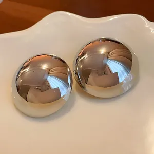 Close-up of chunky silver-toned dome stud earrings with reflective mirror finish