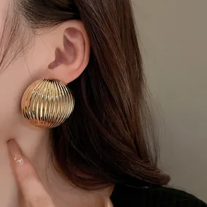 Close-up of gold semi-circular metal earrings with a vertical striped texture on a model's ear.