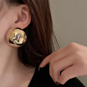 Detailed close-up shot of a glossy gold metallic hemispherical stud earring worn on model's ear