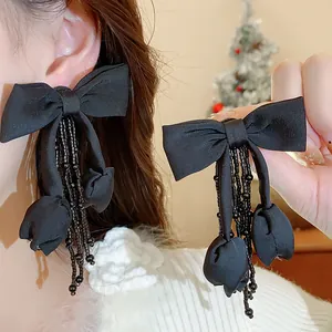 Dettaglio orecchini a fiocco in tessuto nero con nappe di perline e ciondoli a tulipano