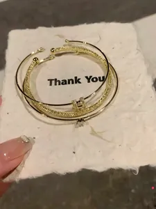 Dettaglio di set di tre bracciali rigidi placcati in oro con lettera H e zirconi