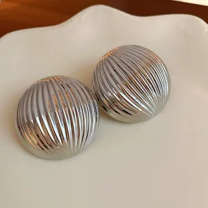 Close-up detail of stylish silver metallic ribbed dome stud earrings on white ceramic.