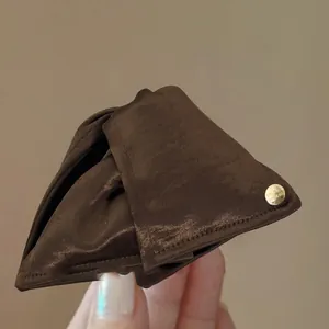 Dettaglio di una molletta per capelli a triangolo in raso marrone con tag d'oro