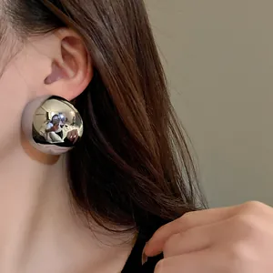 Detailed close-up view of a large silver metallic dome earring worn on a model's ear.