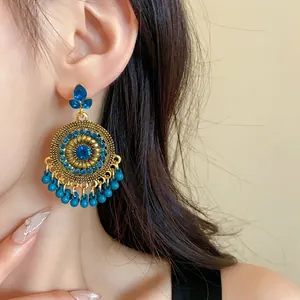 Bohemian ethnic gold-tone earrings with blue rhinestones and tassels worn by a model