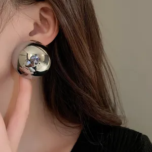 A detailed close-up view of a large silver metallic ball stud earring on model