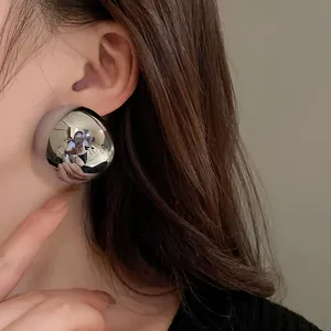Detail of minimalist metallic semi-sphere stud earrings worn on a model's ear, silver needle