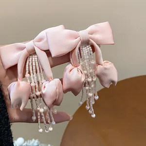 Dettaglio di orecchini a fiocco in tessuto rosa con nappine di perle e tulipani