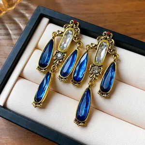 Close-up of vintage water drop tassel earrings with blue crystals and gold finish