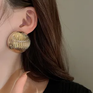 Close-up of metallic ribbed half-round gold stud earrings worn by model.